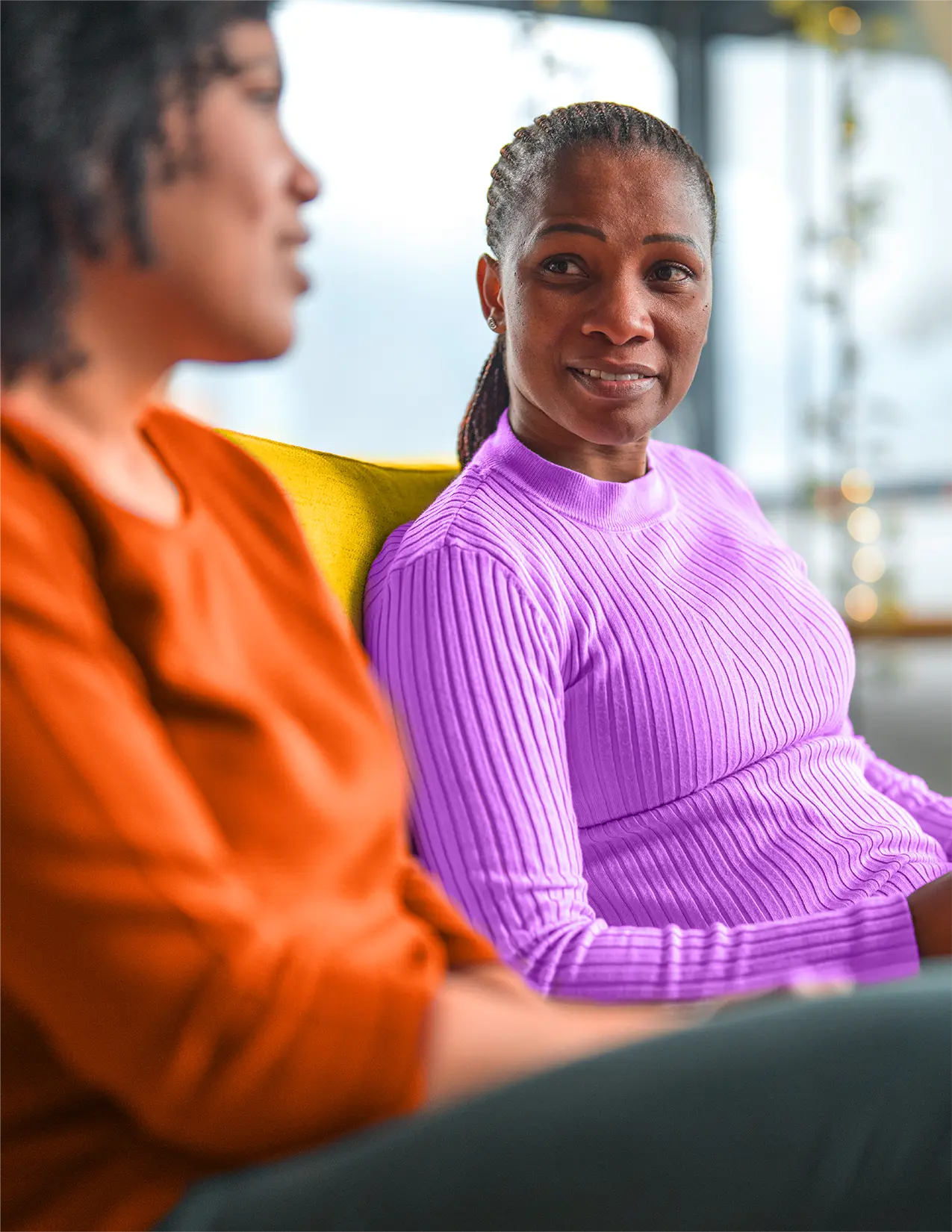 Two African-American women sitting on a yellow couch talking