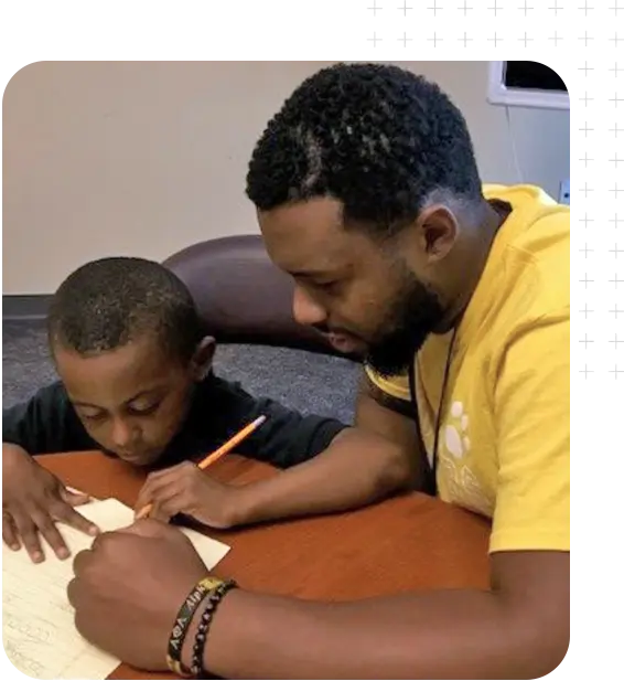 A man in a yellow shirt helping a young student with homework