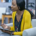 African-American woman wearing a yellow sweater taking notes on a clipboard