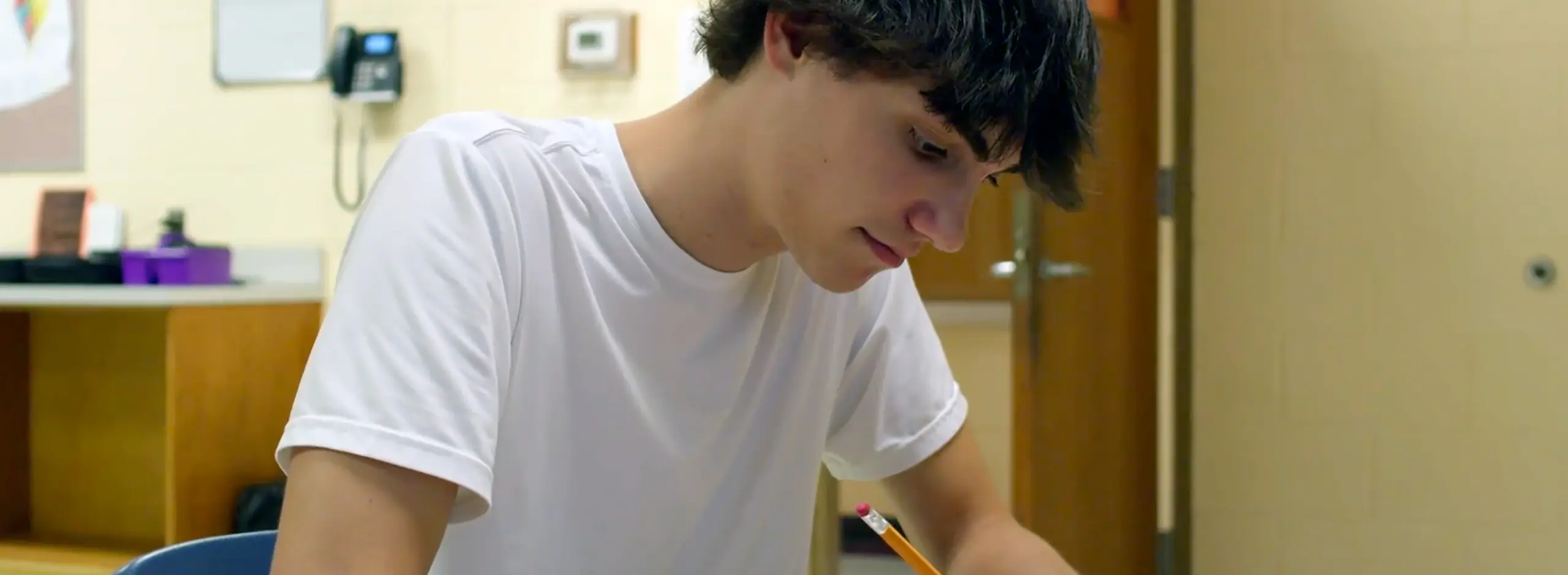 Teenage boy sitting at a school desk writing on a piece of paper